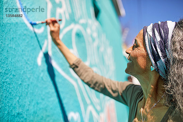 Ältere Frau malt Wandgemälde an einer sonnigen Wand