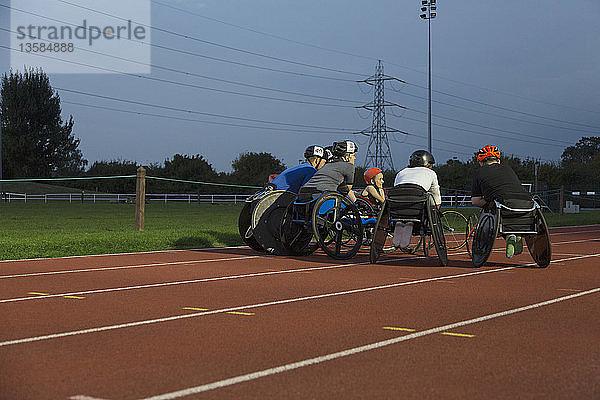 Querschnittsgelähmte Athleten kauern auf einer Sportbahn und trainieren nachts für ein Rollstuhlrennen