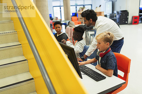 Lehrerin hilft Schülern der Mittelstufe bei der Benutzung der Computer in der Bibliothek