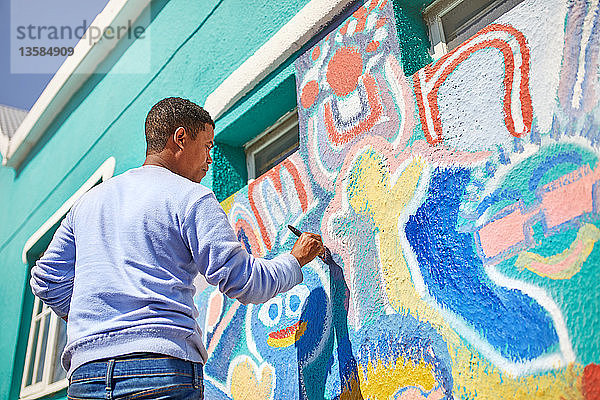 Männlicher Freiwilliger malt ein lebendiges Wandgemälde an eine sonnige Wand
