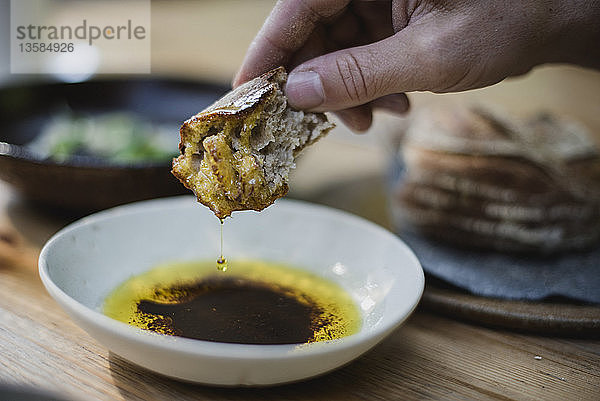 Nahaufnahme: Hand taucht Brot in Olivenöl und Balsamico-Essig