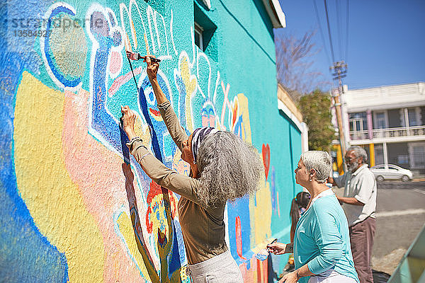 Freiwillige Senioren malen ein lebendiges Wandgemälde auf eine sonnige Stadtmauer