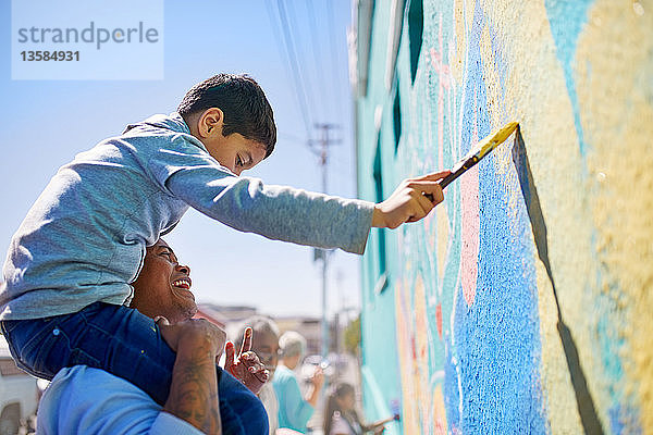 Vater und Sohn malen als Freiwillige ein Wandgemälde an eine sonnige Wand