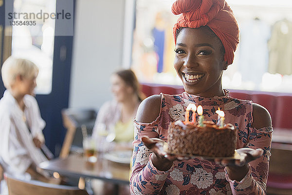 Porträt einer lächelnden  selbstbewussten jungen Frau  die einen Geburtstagskuchen mit Kerzen hält