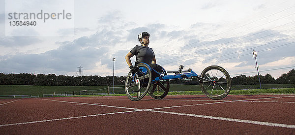 Entschlossene junge querschnittsgelähmte Sportlerin trainiert für ein Rollstuhlrennen auf einer Sportbahn