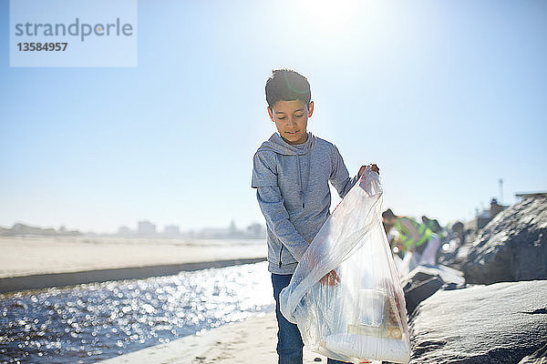 Freiwilliger Junge räumt Müll am sonnigen Strand auf