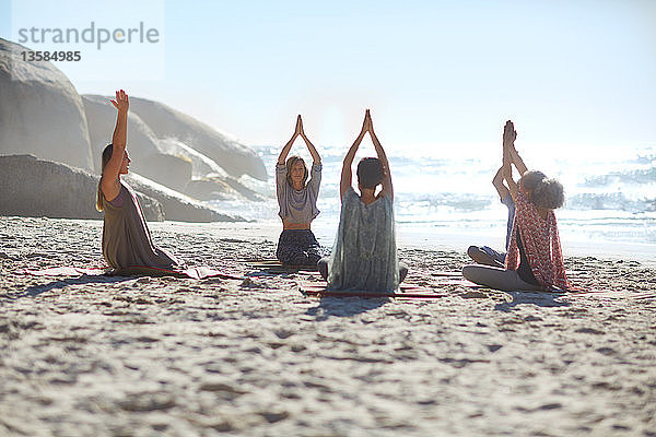 Gelassene Menschen im Kreis meditieren am sonnigen Strand während eines Yoga-Retreats