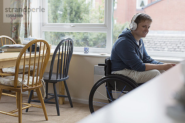 Junge Frau im Rollstuhl hört mit Kopfhörern am Fenster Musik