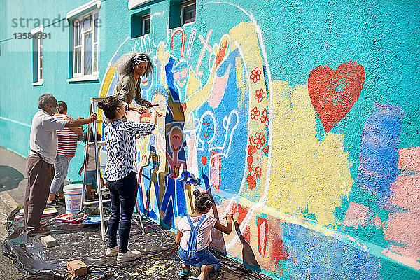 Freiwillige aus der Gemeinschaft malen ein buntes Wandgemälde auf eine sonnige Stadtmauer