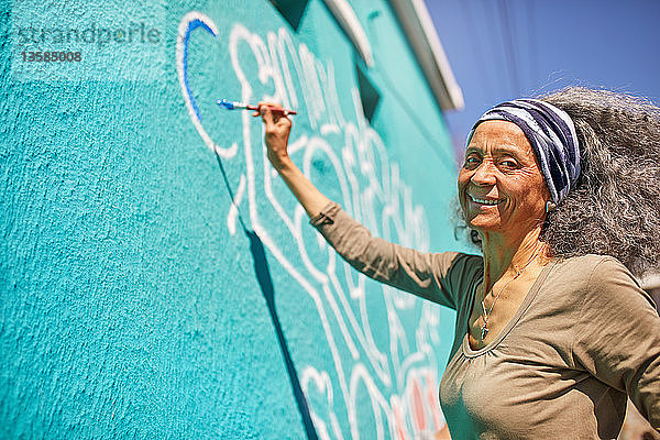 Porträt glücklicher älterer weiblicher Freiwilliger  der an einer sonnigen Wand malt
