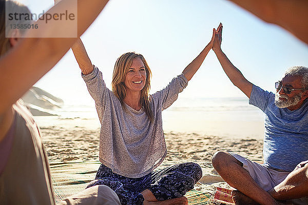Glückliche Freunde  die sich während eines Yoga-Retreats am sonnigen Strand im Kreis an den Händen fassen