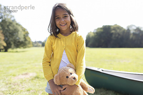 Portrait lächelndes  süßes Mädchen mit Teddybär in sonnigem Feld