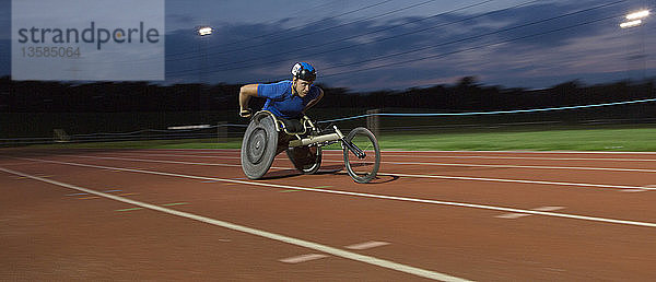 Entschlossener junger querschnittsgelähmter Sportler  der bei einem nächtlichen Rollstuhlrennen über eine Sportstrecke rast