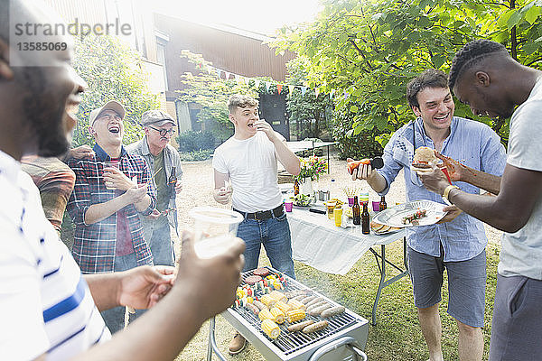 Männliche Freunde lachen und essen um einen Grill im Hinterhof