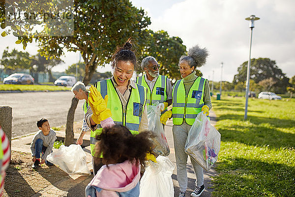 Fröhliche Freiwillige  die sich gegenseitig zujubeln und den Müll im sonnigen Park beseitigen
