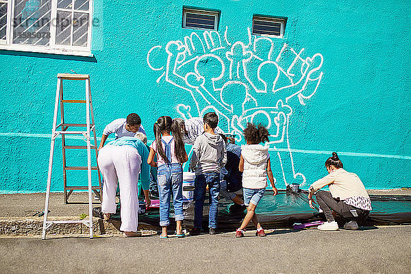 Freiwillige Kinder malen ein Wandgemälde auf einer sonnigen Mauer