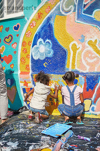 Mädchen malen ein lebendiges Wandgemälde an eine sonnige Wand