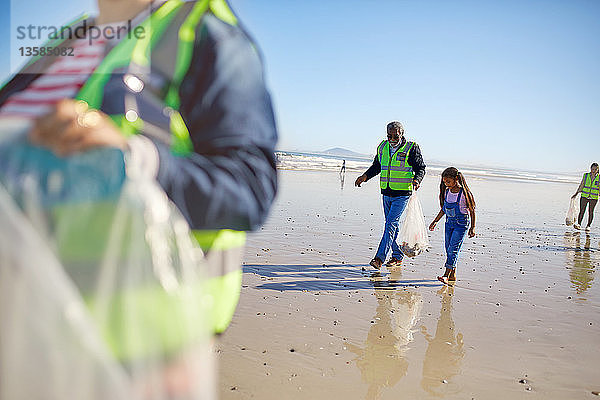 Großvater und Enkelin beseitigen freiwillig Müll am sonnigen  nassen Sandstrand