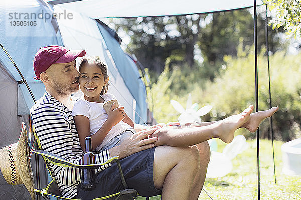 Glücklicher  liebevoller Vater hält seine Tochter auf dem Schoß auf einem sonnigen Campingplatz