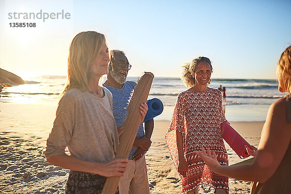 Lächelnde Freunde mit Yogamatten am sonnigen Strand während eines Yoga-Retreats