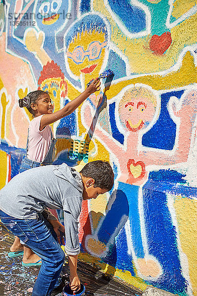 Kinder malen ein lebendiges Wandgemälde an eine sonnige Wand