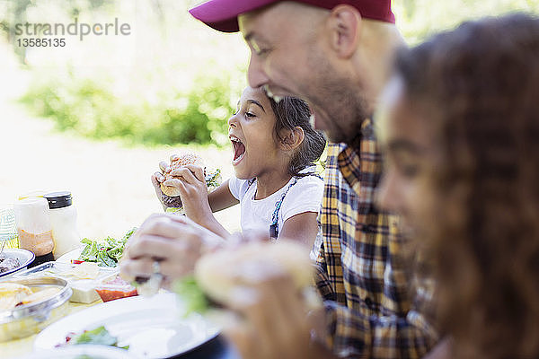 Verspielter Vater und Tochter essen Grillhamburger auf dem Campingplatz