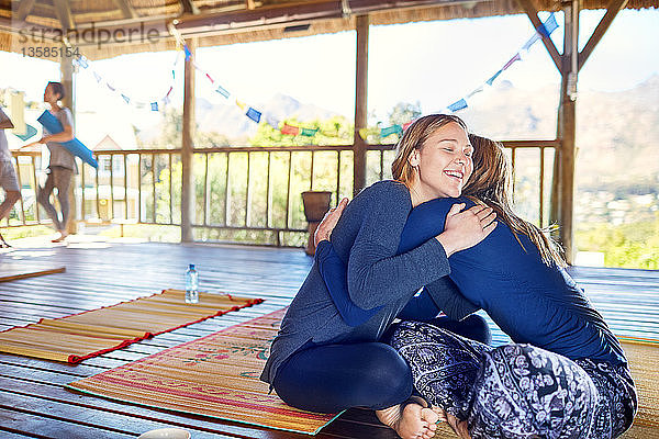 Glückliche Mutter und Tochter umarmen sich auf Yogamatten in einer Hütte während eines Yoga-Retreats