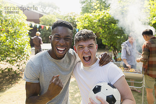 Porträt begeisterter junger Männer mit Fußball  die jubelnd im Hinterhof grillen