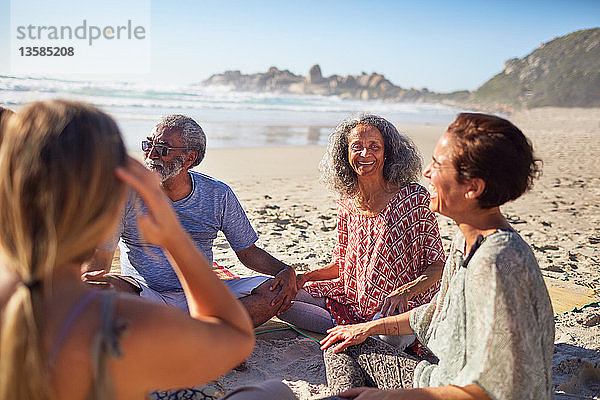 Freunde sitzen im Kreis am sonnigen Strand während eines Yoga-Retreats