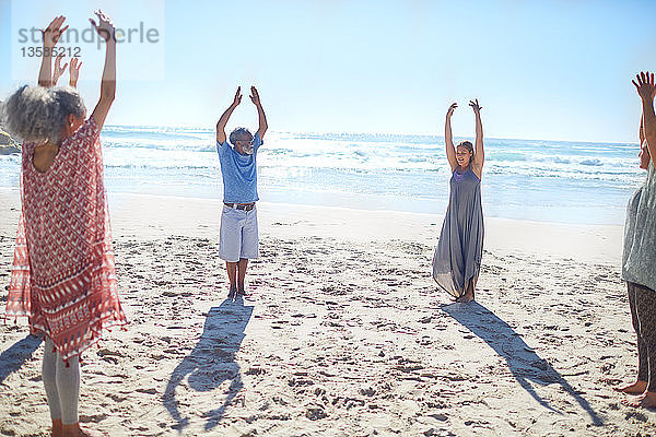 Gruppe steht mit erhobenen Armen im Kreis am sonnigen Strand während eines Yoga-Retreats