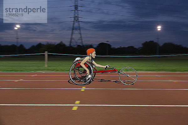 Jugendliche querschnittsgelähmte Sportlerin im Rollstuhl fährt nachts auf einer Sportbahn