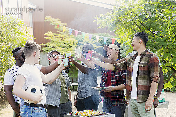 Glückliche männliche Freunde stoßen mit Getränken am Grill im Hinterhof an