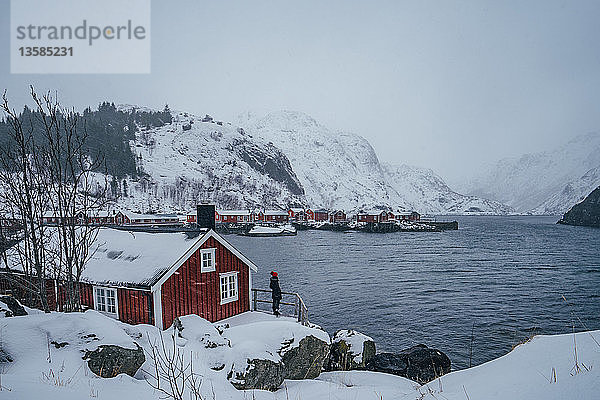 Frau genießt die ruhige Aussicht auf die verschneiten Berge vom Fischerdorf am Wasser aus  Lofoten  Norwegen