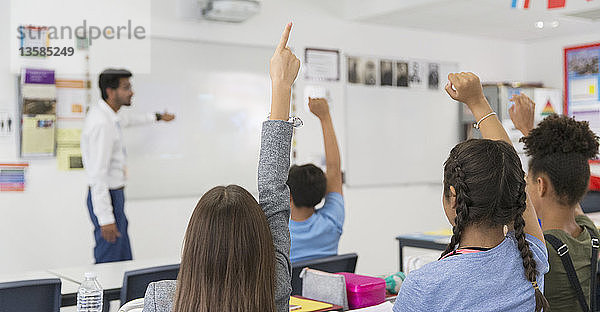 Schüler der Junior High School mit erhobenen Händen während des Unterrichts im Klassenzimmer