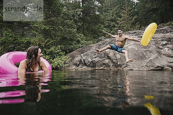 Verspielter junger Mann mit aufblasbarem Ring  der in einen abgelegenen See springt  Squamish  British Columbia  Kanada