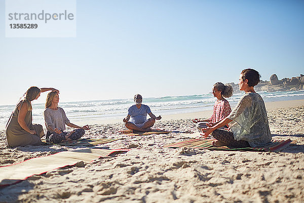 Meditierende Gruppe am sonnigen Strand während eines Yoga-Retreats