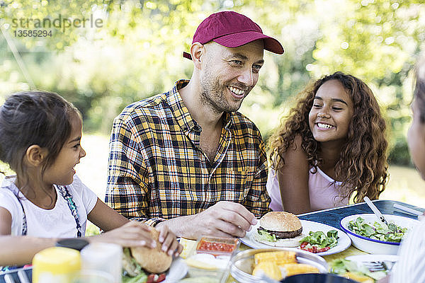 Ein glücklicher Vater und seine Töchter genießen das Mittagessen vom Grill