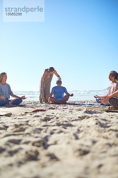 Gelassene Menschen meditieren am sonnigen Strand während eines Yoga-Retreats