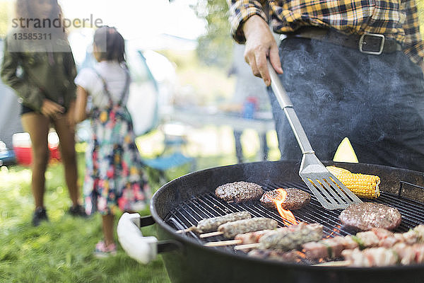 Mann beim Grillen von Hamburgern  Spießen und Maiskolben