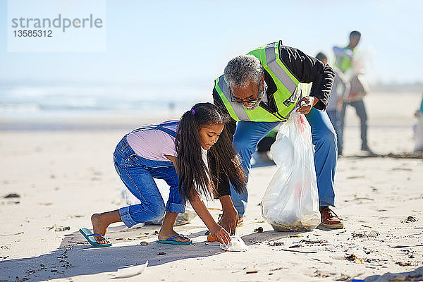 Großvater und Enkelin beseitigen freiwillig Müll am sonnigen Sandstrand