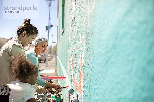 Weibliche Freiwillige malen ein Wandgemälde an eine sonnige Wand
