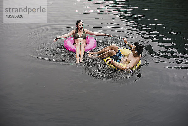Junges Paar schwimmt in aufblasbaren Ringen auf dem See