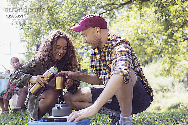 Tochter schenkt ihrem Vater am Campingkocher Kaffee aus einem isolierten Getränkebehälter ein
