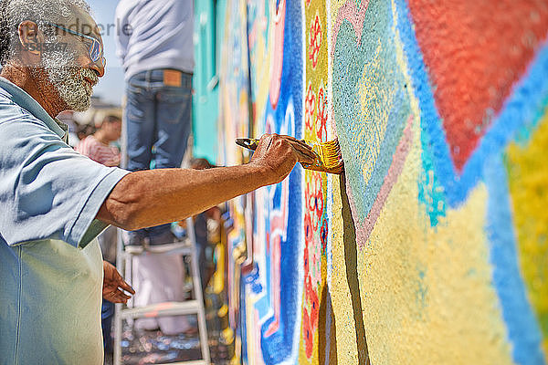 Älterer Mann malt Wandbild an sonniger Wand