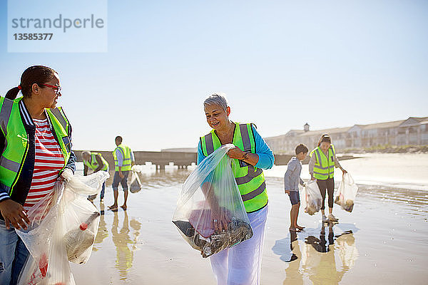 Freiwillige beseitigen Müll am sonnigen  nassen Sandstrand