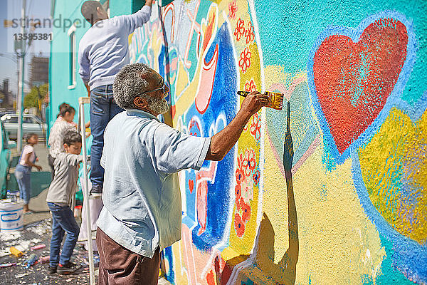 Ein älterer Mann malt ein Wandgemälde auf einer sonnigen Stadtmauer