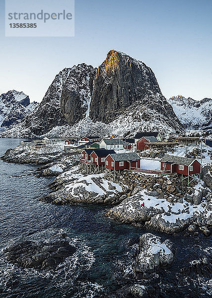 Beschauliches  schneebedecktes Fischerdorf und Klippen am Wasser  Hamnoy  Lofoten  Norwegen