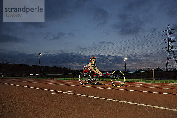 Porträt eines selbstbewussten  querschnittsgelähmten Mädchens  das auf einer nächtlichen Sportbahn für ein Rollstuhlrennen trainiert