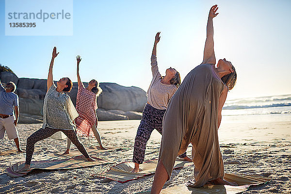 Gruppe beim Üben der umgekehrten Kriegerpose am sonnigen Strand während eines Yoga-Retreats