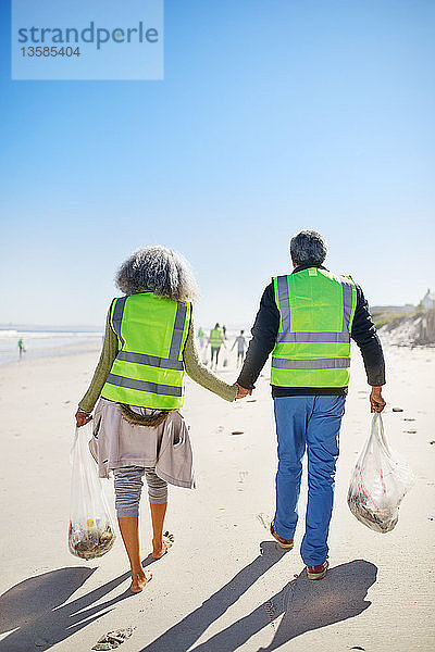 Liebevolles Seniorenpaar räumt freiwillig Müll am sonnigen  nassen Sandstrand auf